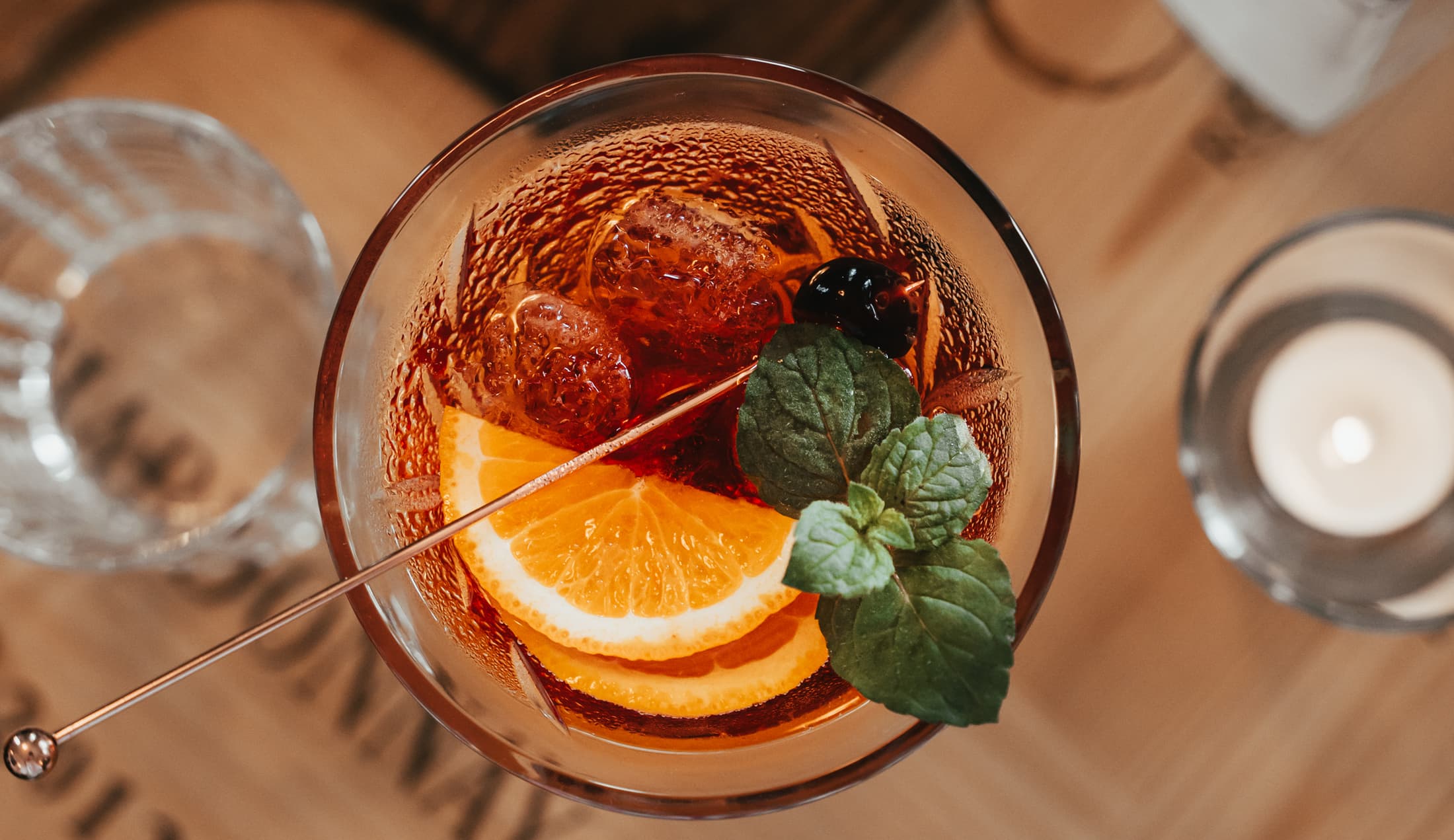 Ein Aperitif mit Orangenscheibe und Minze von oben, daneben ein Wasserglas und eine Kerze