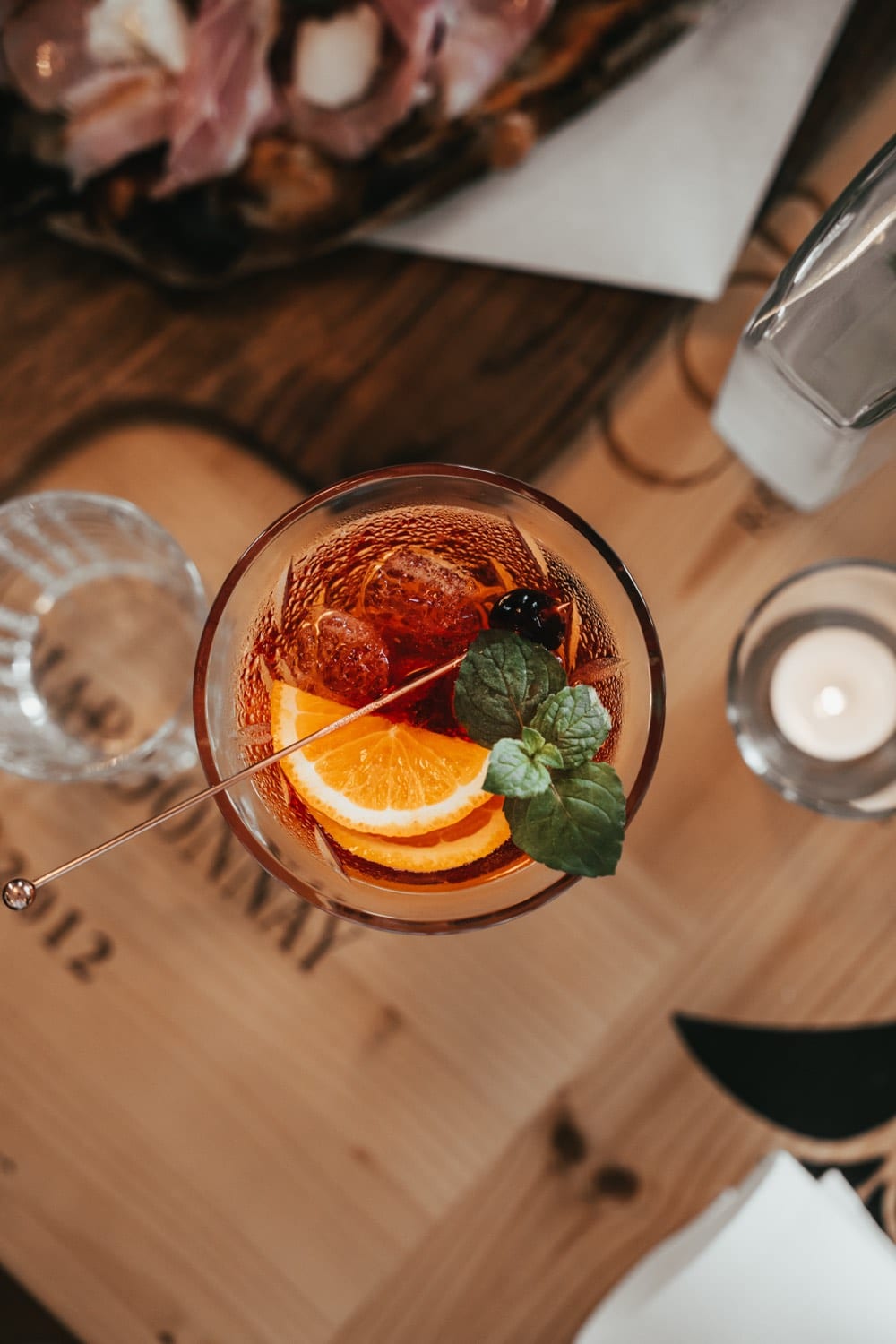 Ein Aperitif mit Orangenscheibe und Minze von oben auf einem Holztisch, daneben eine Kerze