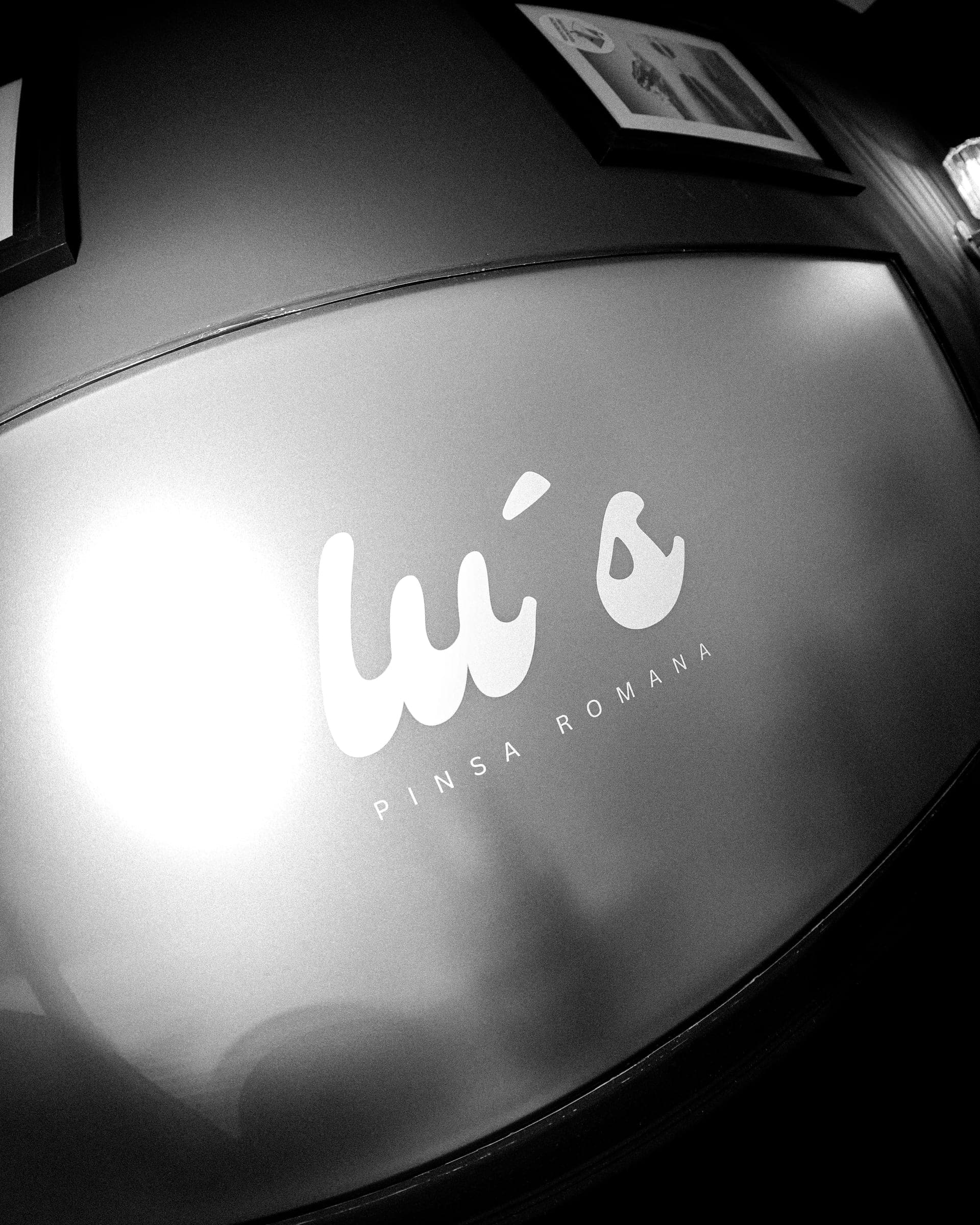 Das Lu’s-Logo auf einer Milchglastür, gerahmt von der Wand des Gastraums
